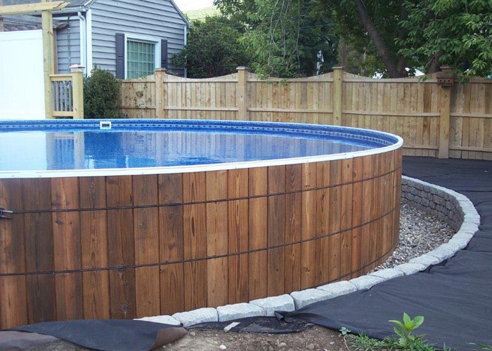 wooden round above ground pool surrounded by stone