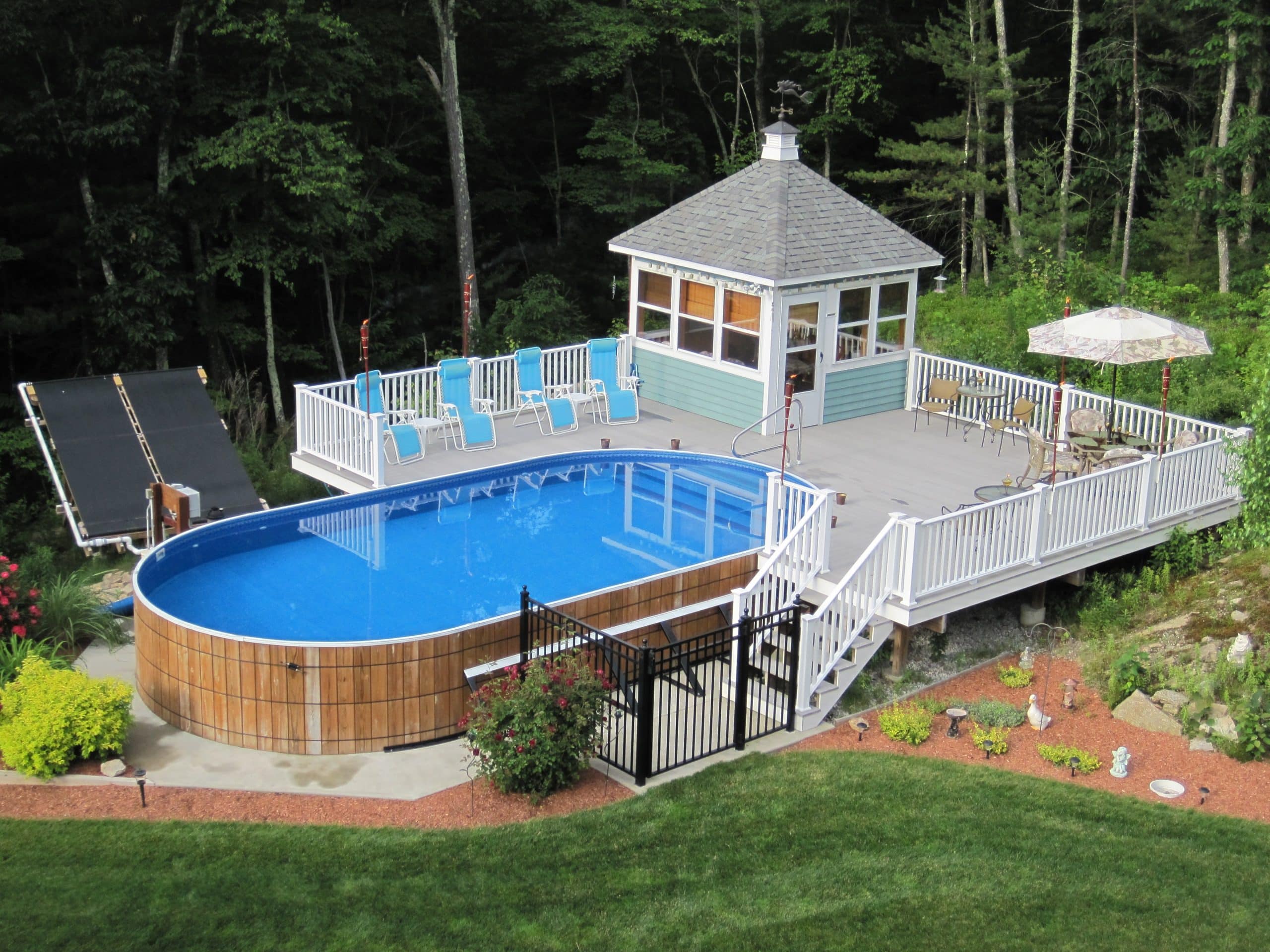 oval wooden above ground pool with deck and cabana